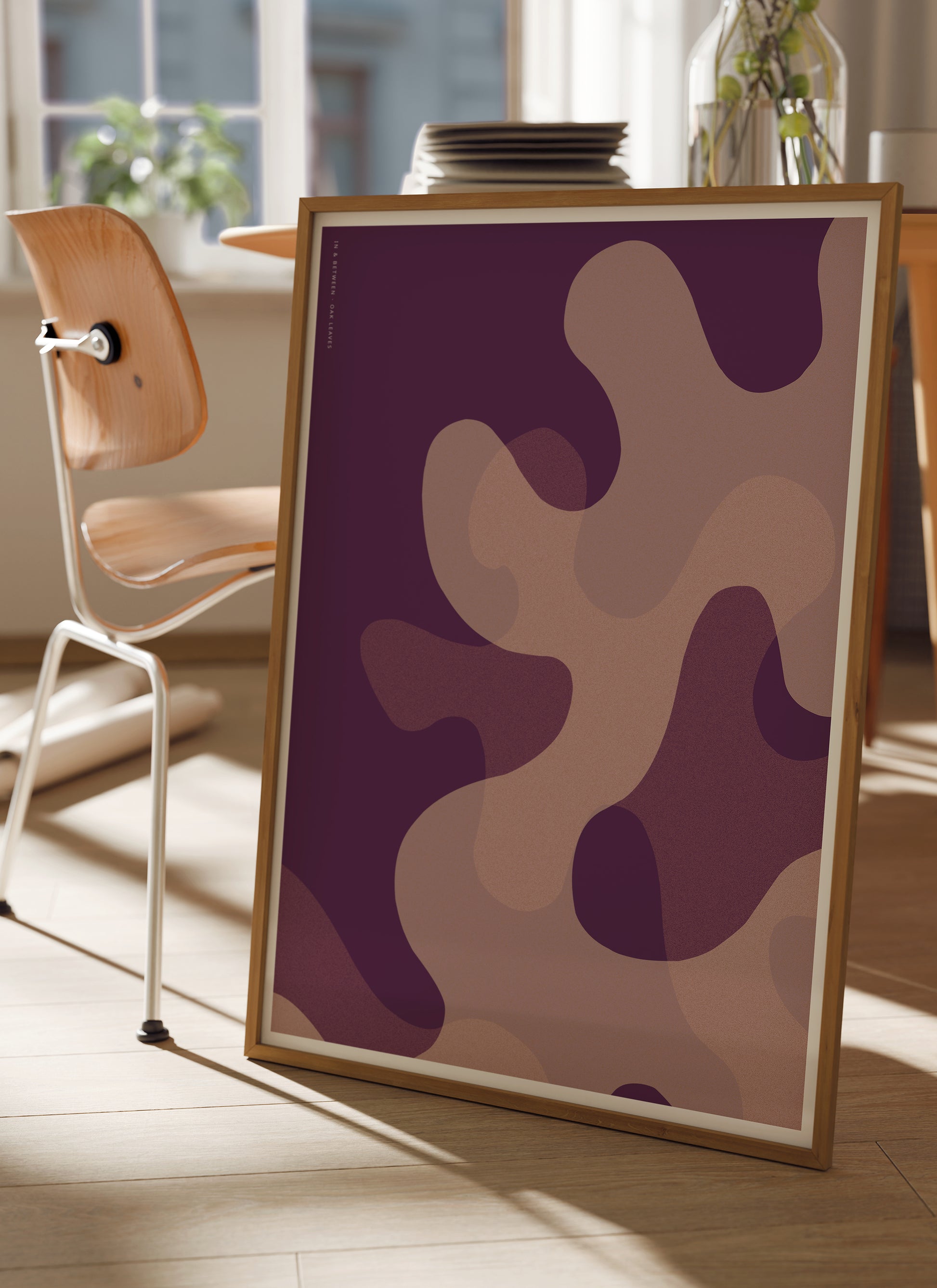 Lifestyle image with art print of large warm violet oak leaf shapes in natural wooden frame.